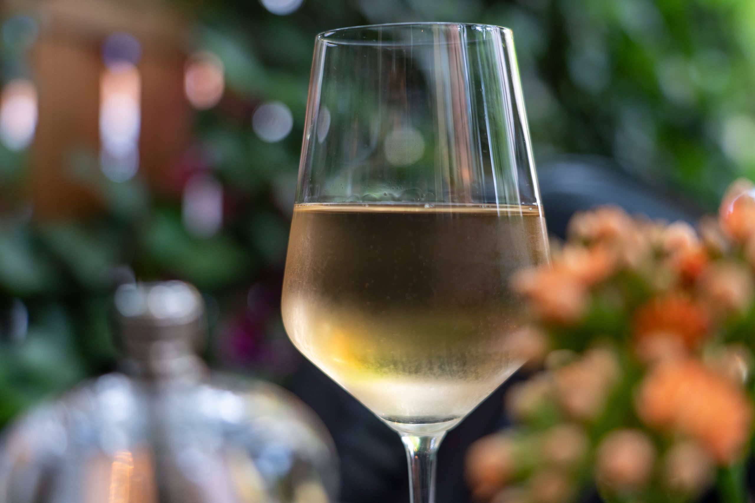 Close up of a glass of white Viognier wine with flowers out of focus in the background.
